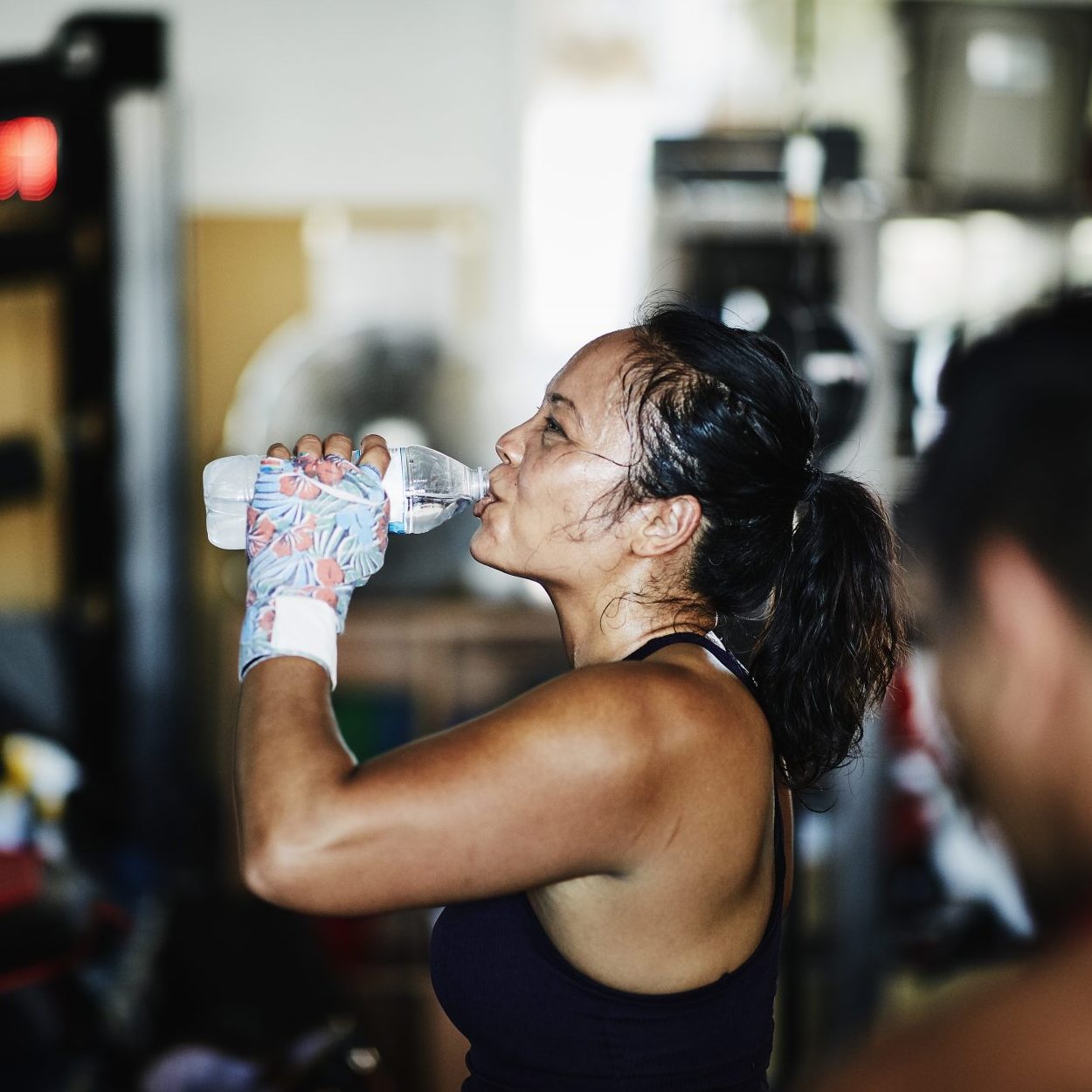 Sweating female boxer drinking water after workout in boxing gym