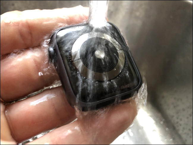 An Apple Watch being rinsed under running water.