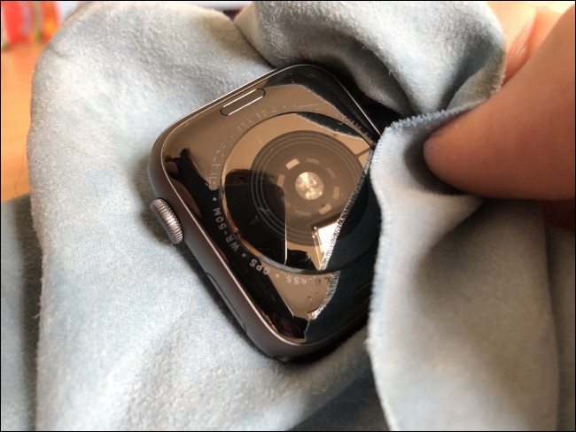 A hand wiping an Apple Watch with a cloth.