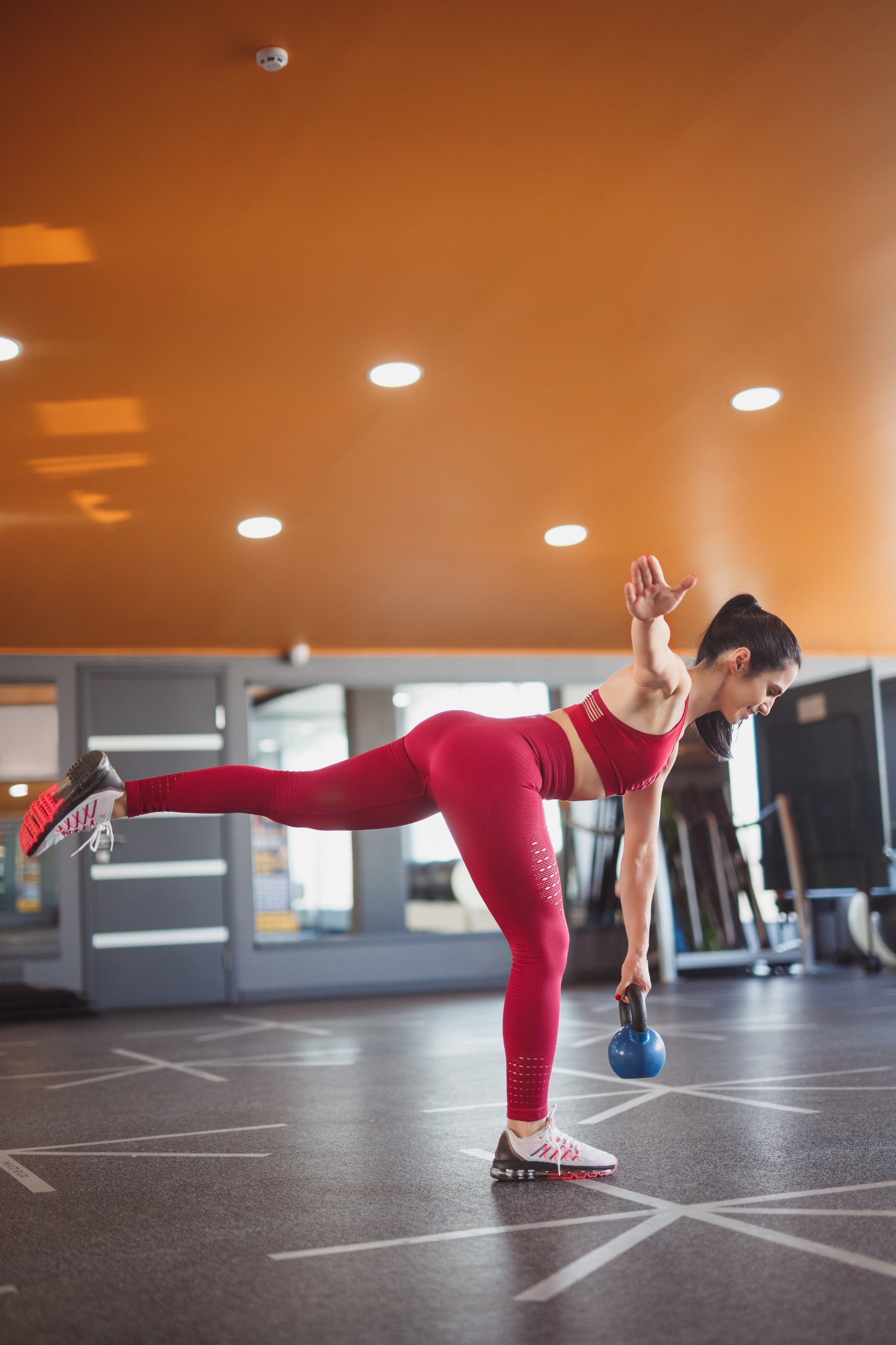 Side view of woman doing single leg kettlebell deadlift standing in modern gym and balancing