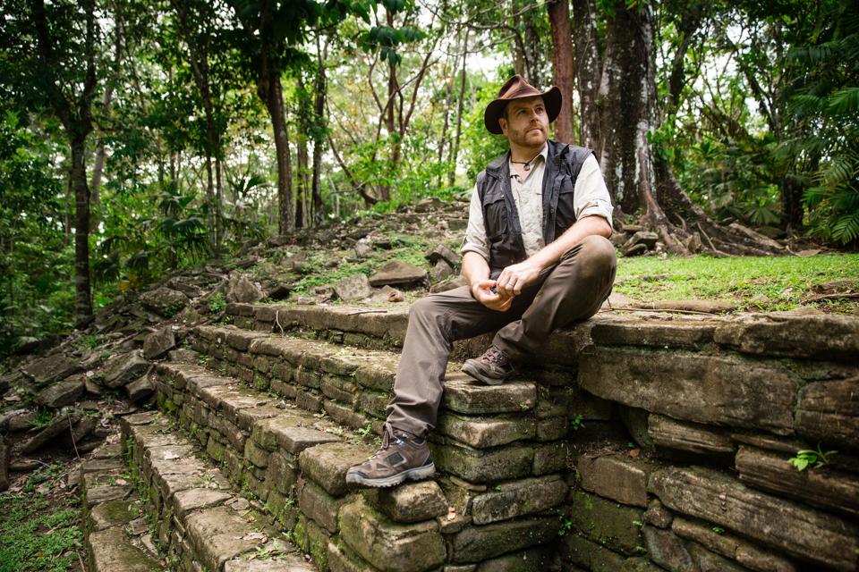 An explorer sits atop the ruins of a Mayan pyramid in the green jungles of Belize.